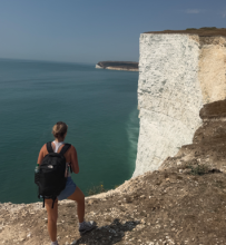 A UO student standing on gravel, looking at the Seven sisters cliff