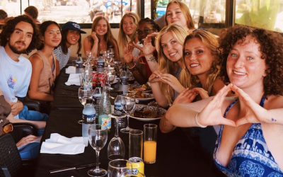 Group of college students at a restaurant table holding up the University of Oregon's hand sign, the letter "O."