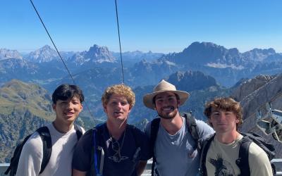 Four college-aged males posing in front of a mountain background. 