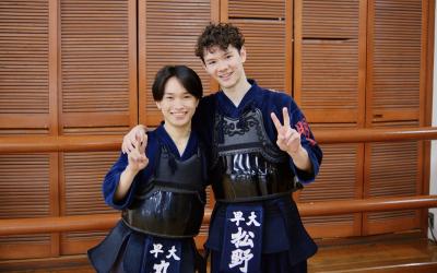 Two young males wearing traditional Japanese Kendo uniforms holding up peace signs. 