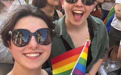 Two people attending a Pride parade in Lecce, Italy. One is holding a small Pride flag. 