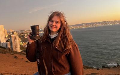 College-aged woman posing on a beach in Chile during sunset holding up a professional camera. 