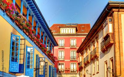 Colorful buildings with balconies adorned with flowers under a clear sky in a town square in Spain.