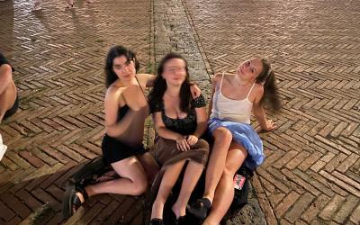 Three people sitting on a cobblestone street at night, smiling and posing for a photo.