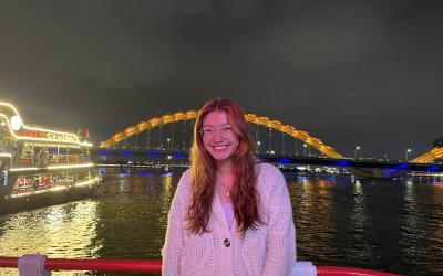 Smiling person on a boat with the Dragon Bridge illuminated in the background in Da Nang, Vietnam at night.