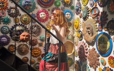 A person exploring a vibrant shop decorated with colorful, assorted sun and moon face masks on the walls.