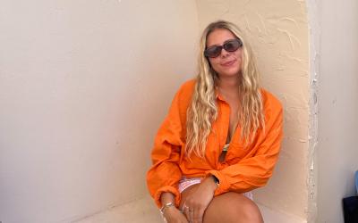 College-aged girl in an orange top wearing sunglasses posing for a picture. 