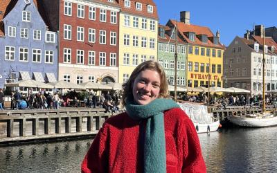 College-aged female smiling in front of line of colorful houses along the waterfront in Denmark.