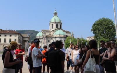 Students stand around a staff member, who is sharing about the buildings nearby in the outdoor square