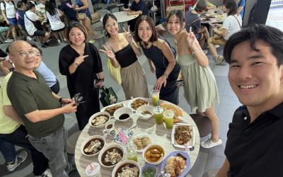 Logan and five others stand around a circular table with many plates of food