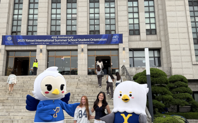 Megan and her roommate stand outside of a big academic building and pose with two bird mascots, the Yonsei mascots