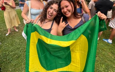 Two people holding a University of Oregon flag on a field of grass. 