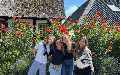 Three girls smiling in front of a bush with flowers. 