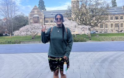 Keke stands in front of a clock tower, holding up a peace sign