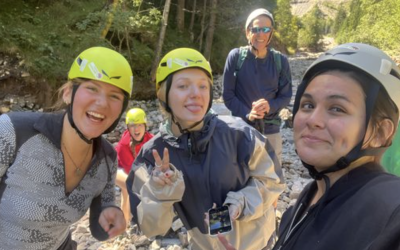 Nathalie and two other program participants wear brightly colored helmets. Rocks and green trees are in the background