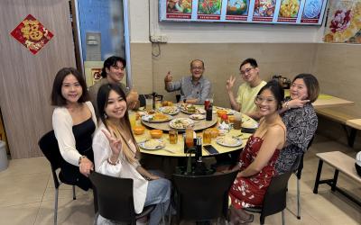 Logan and 6 others sit around a table with plates of singaporean chicken rice