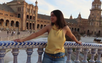 Ava stands on a balcony, with a city building in the background