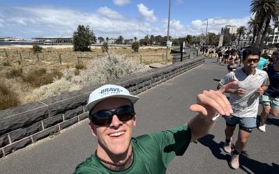 Calvin, in running clothes, a hat, and sunglasses, takes a selfie, with a trail of runners behind him