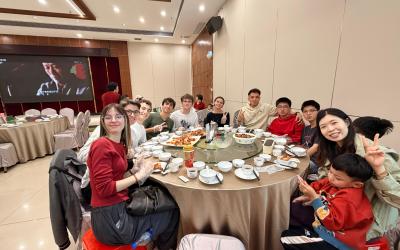 a group of people sit around a large circle table, many dressed in red; they are all smiling and celebrating Chinese New Year