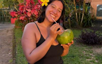 Valeria smiling on the grass in Costa Rica while drinking from a coconut.