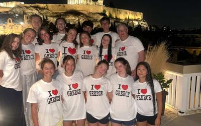 Cohort of GEO students posing for a photo at night wearing matching "I Heart Greece" T-shirts