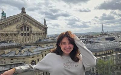Giana smiling on a rooftop in Paris on a cloudy day with the Eiffel tower in the skyline.