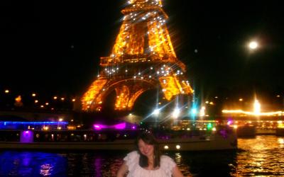 Giana smiling by the River Siene in Paris at night with the Eiffel Tower sparkling in the background