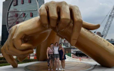 Students standing under a golden statue of two hands