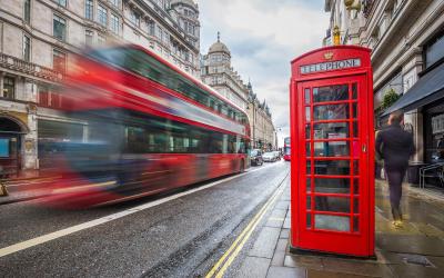 A blurred red double decker bus with a red telephone booth on the right side